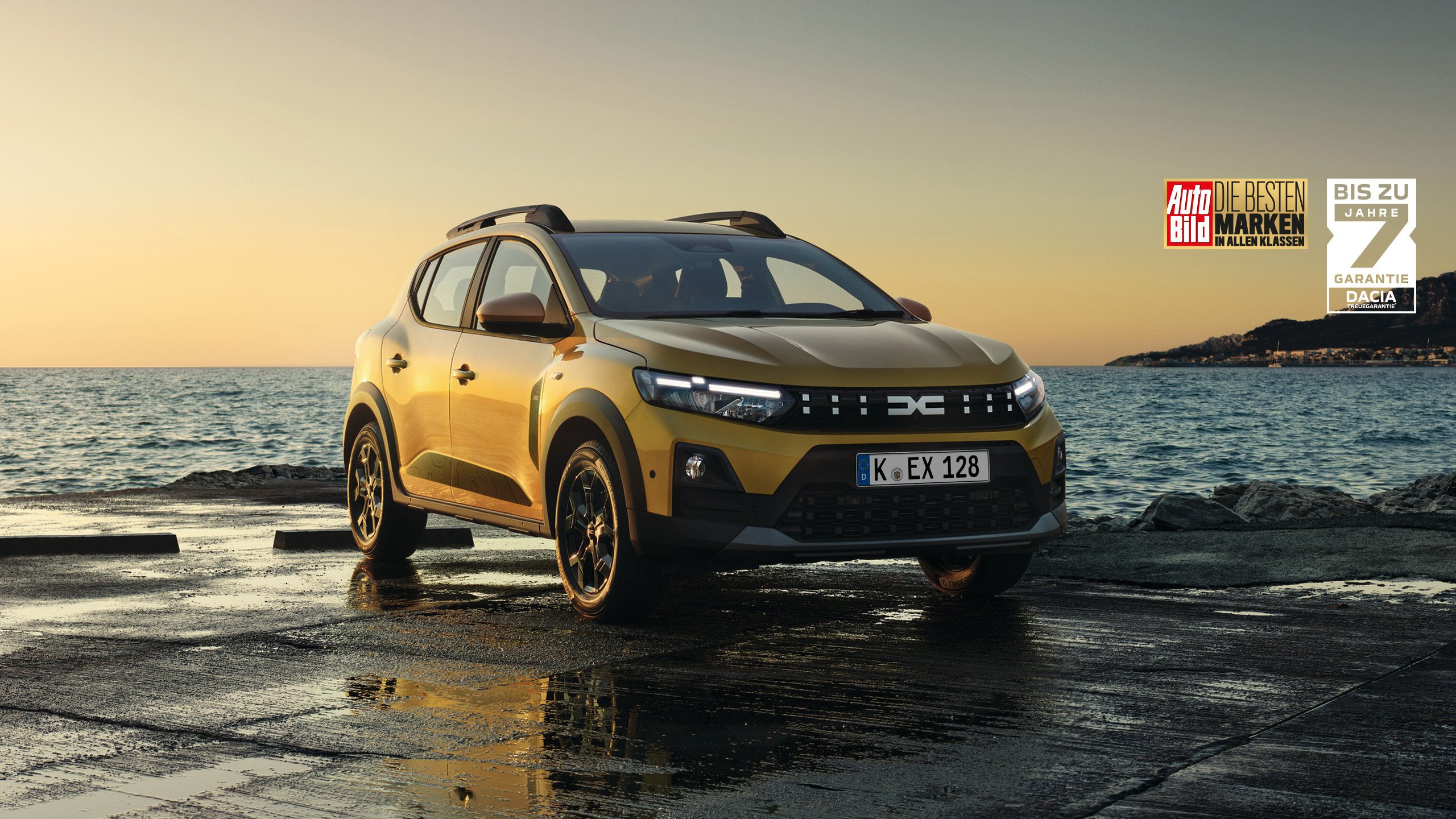 Gelber Dacia Autobild Siegel am Meer bei Sonnenuntergang mit Auto im Vordergrund.